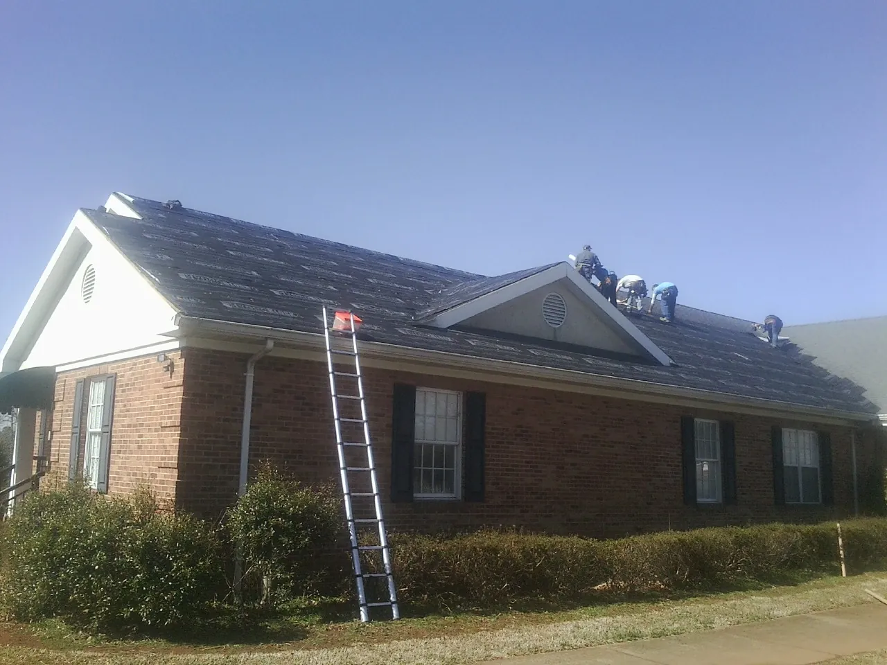 Crew tearing shingles off a brick ranch roof with a ladder set — Metal Roof Repair work by our crew in Lake Winola