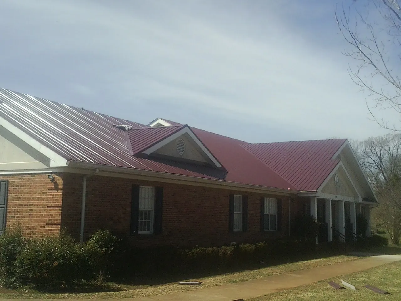 Red metal roof with gabled entries on a long brick building, from a Hail Damage Roof Repair job in Lake Winola