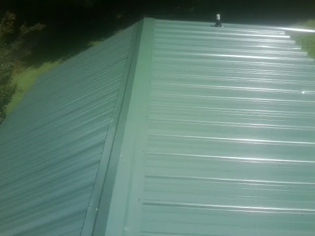New green metal panels meeting at the ridge of a roof — Flat Roof Repair work by our crew in Lake Winola
