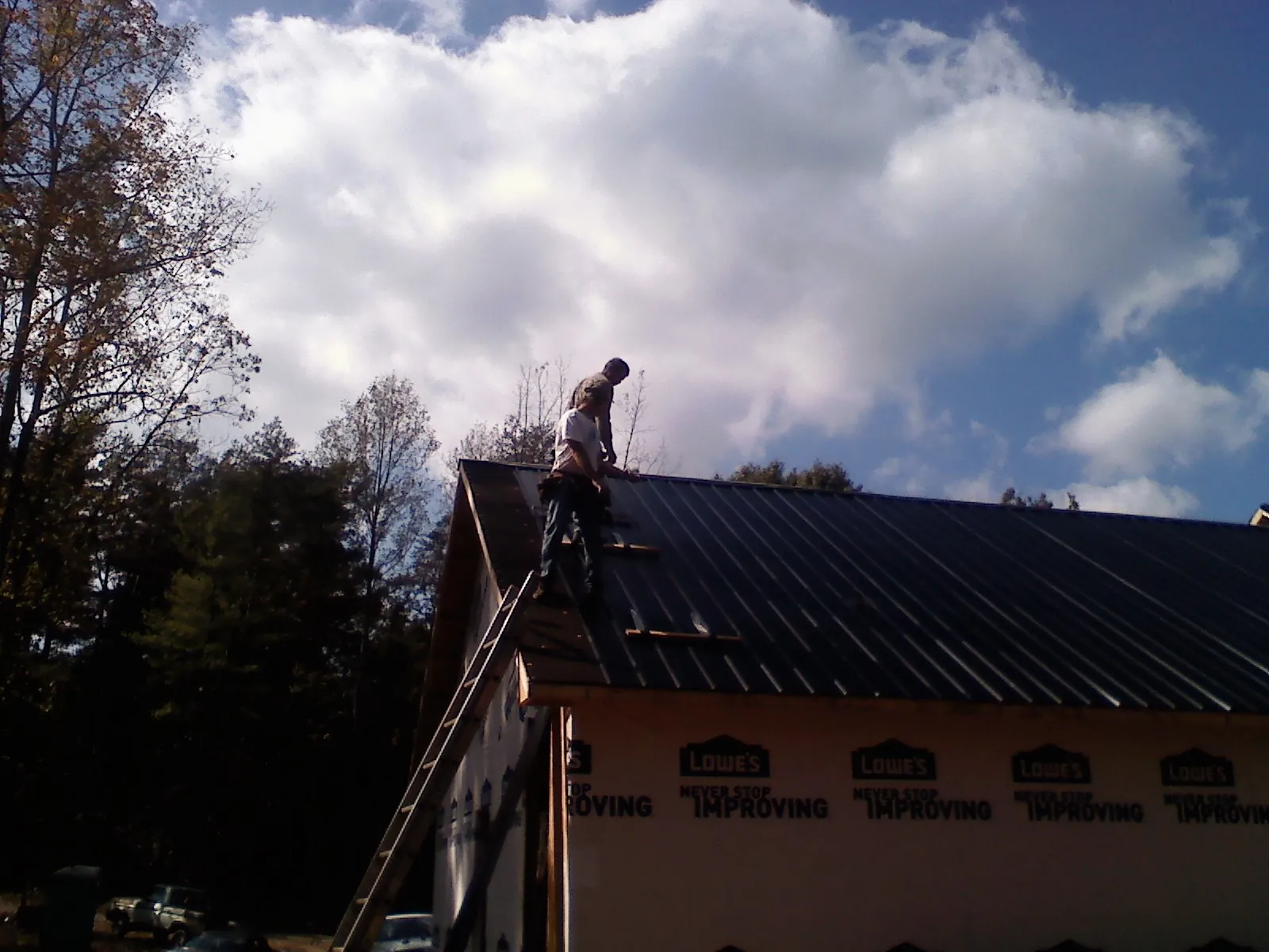Roofer fastening dark metal panels high against a cloudy sky, from a Roof Inspection job in Lake Winola