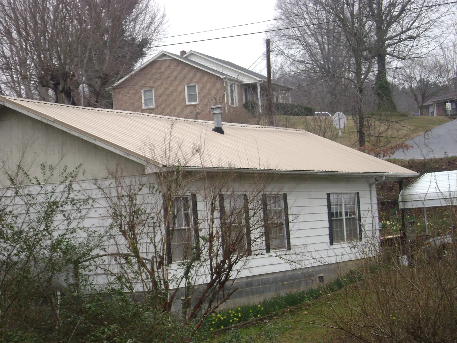 Tan metal roof on a white sided house set into a hillside — Commercial Roofing by Roofing Brothers in Lake Winola